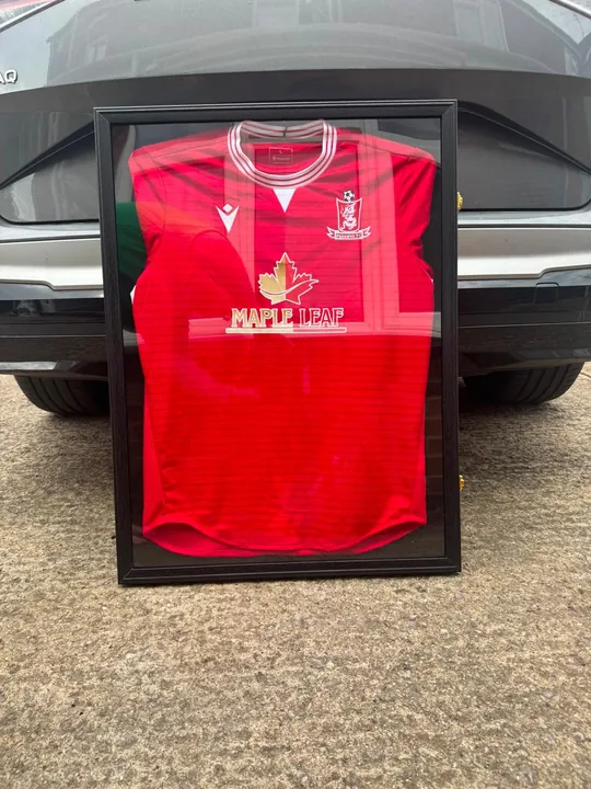 A red Maple Leaf football shirt in a black frame, propped against a car
