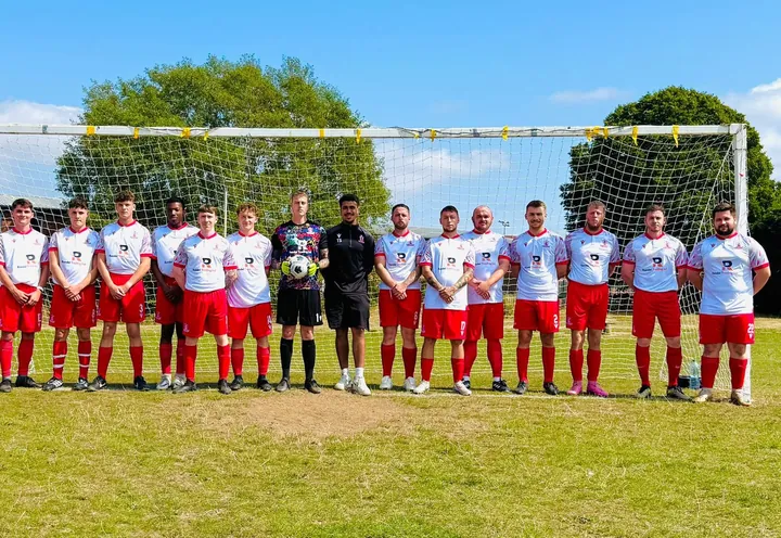 A squad lined up in front of the goal in white shirts and red shorts carrying Rondel Trading Ltd